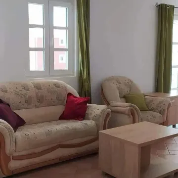 Living room with a sofa set, armchair, coffee table, and a window with green curtains. - image 2