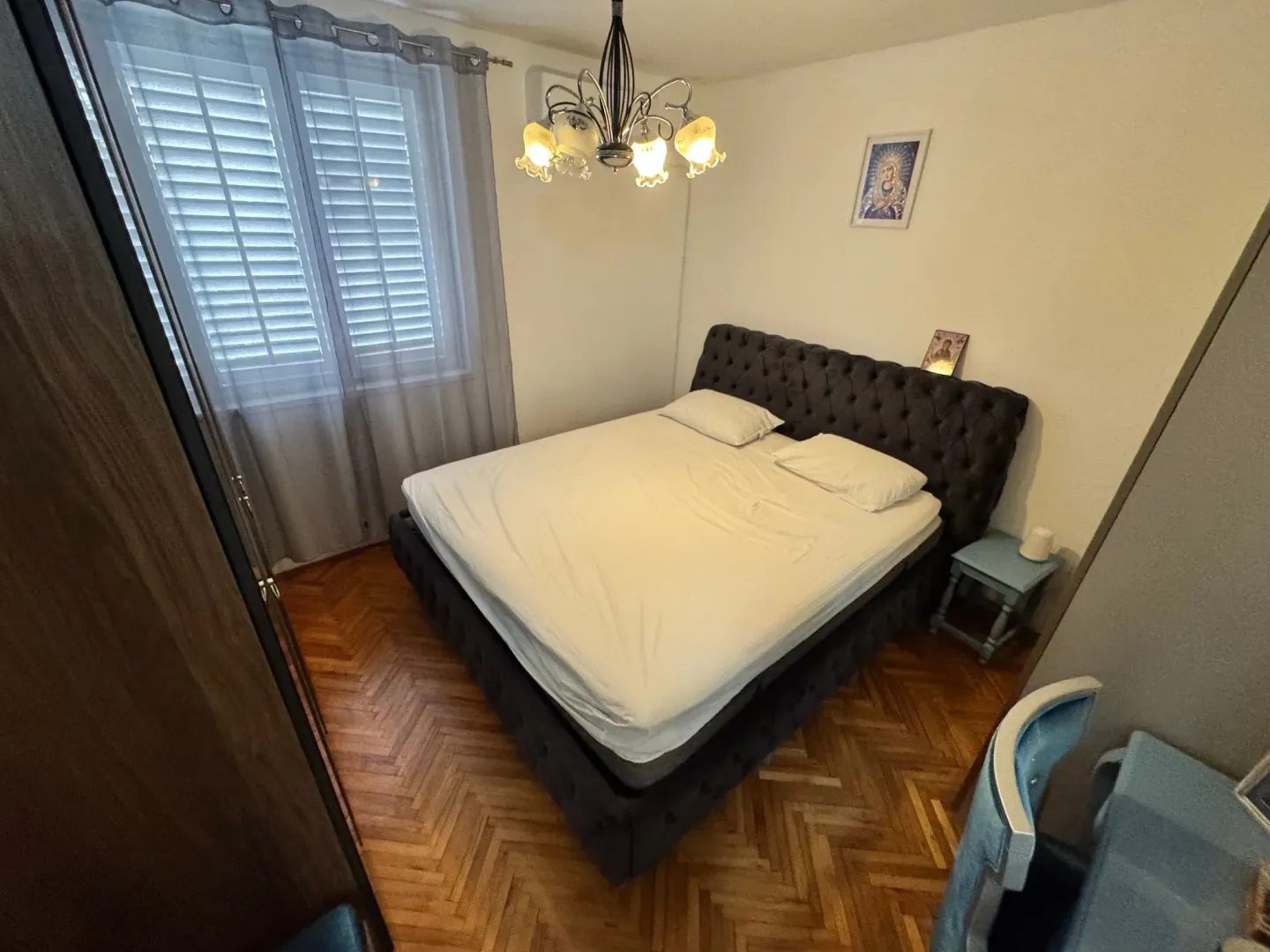 Namještena spavaća soba sa bračnim krevetom, parketom i prozorom.
