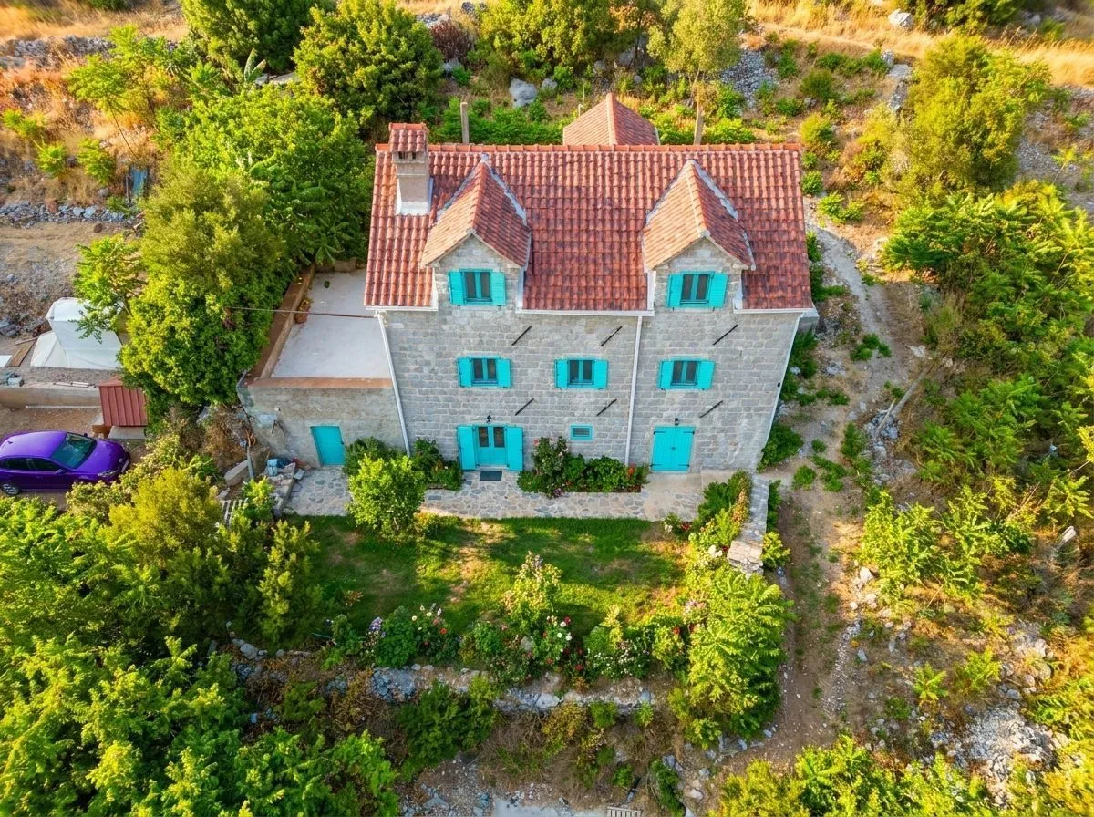 Aerial view of a stone house with a yard and greenery.