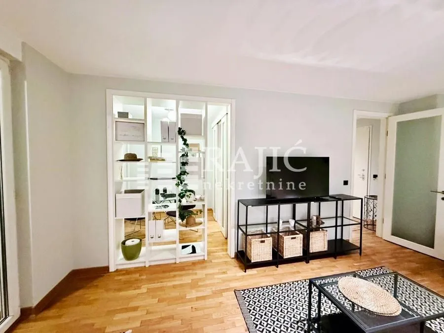 Living room with hardwood flooring and a partition shelving unit leading to a workspace.