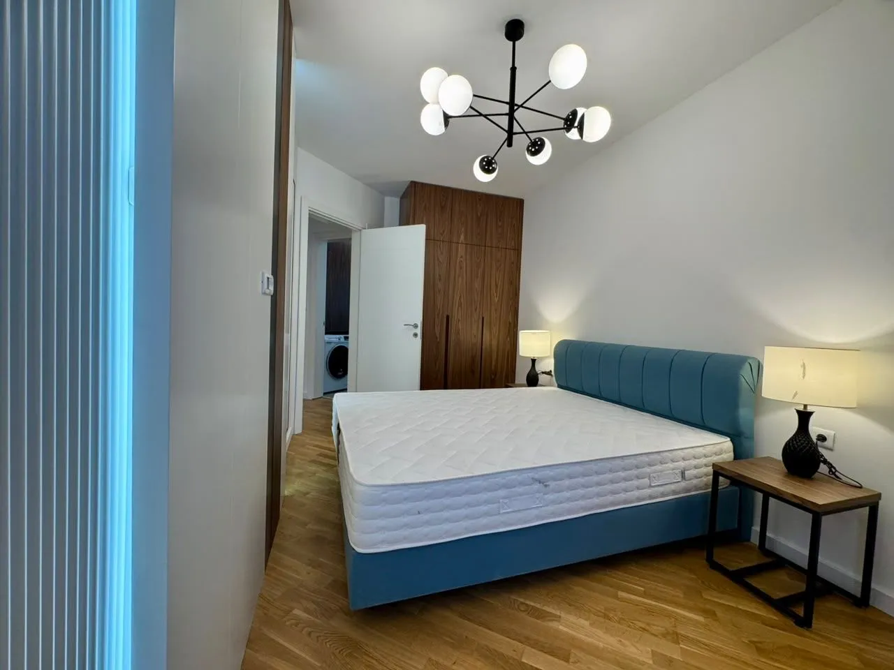 Modern bedroom with a double bed, wooden wardrobe, and parquet flooring.