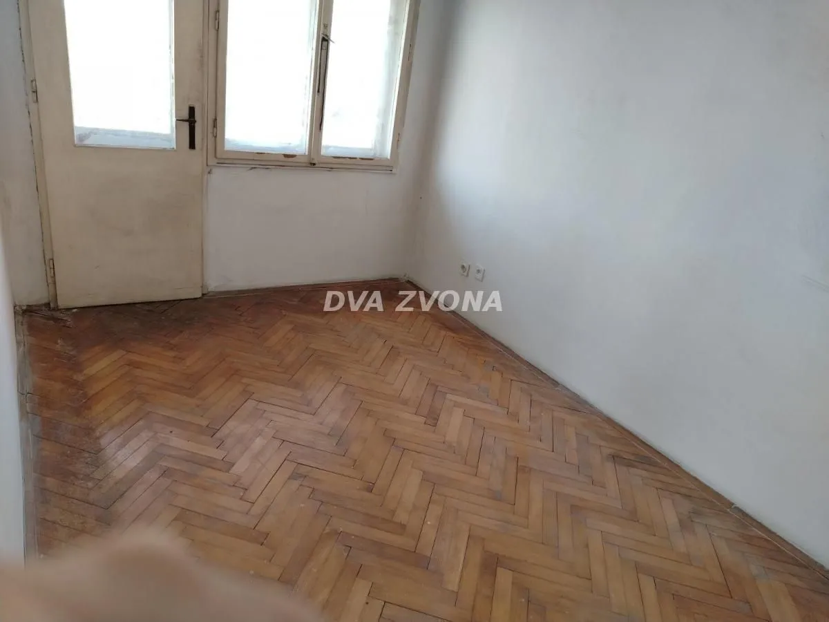 Prazna soba sa drvenim parketom i vratima koja vode na terasu.
