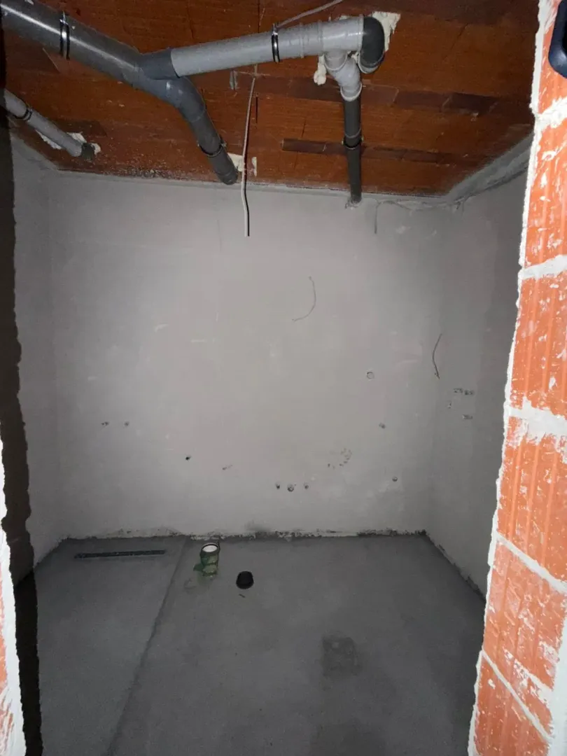 Prazna prostorija u sivoj fazi gradnje sa instalacijama na plafonu.
