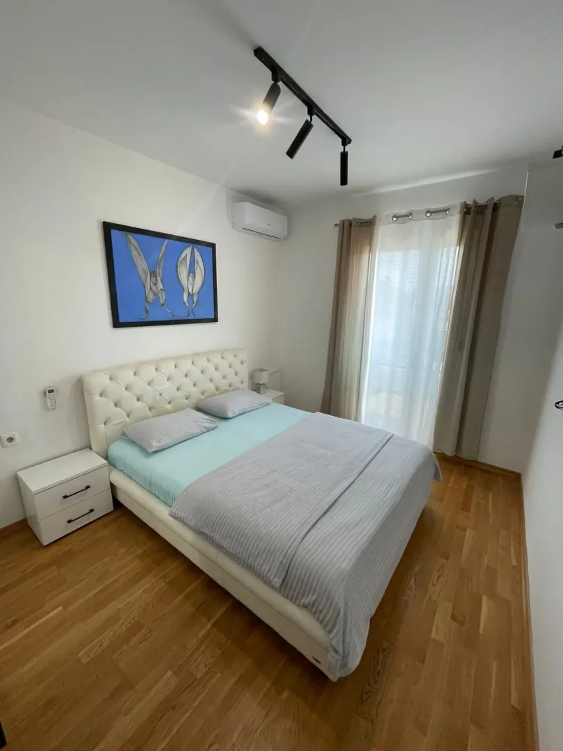 Spavaća soba sa bračnim krevetom, bijelim noćnim ormarićima i laminatnim podom.