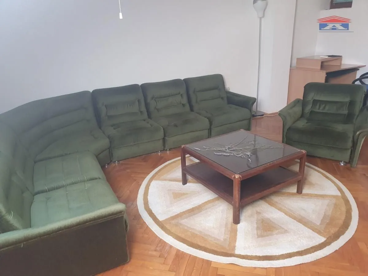 Dnevna soba sa zelenom ugaonom garniturom, foteljom i drvenim stočićem na parketu.