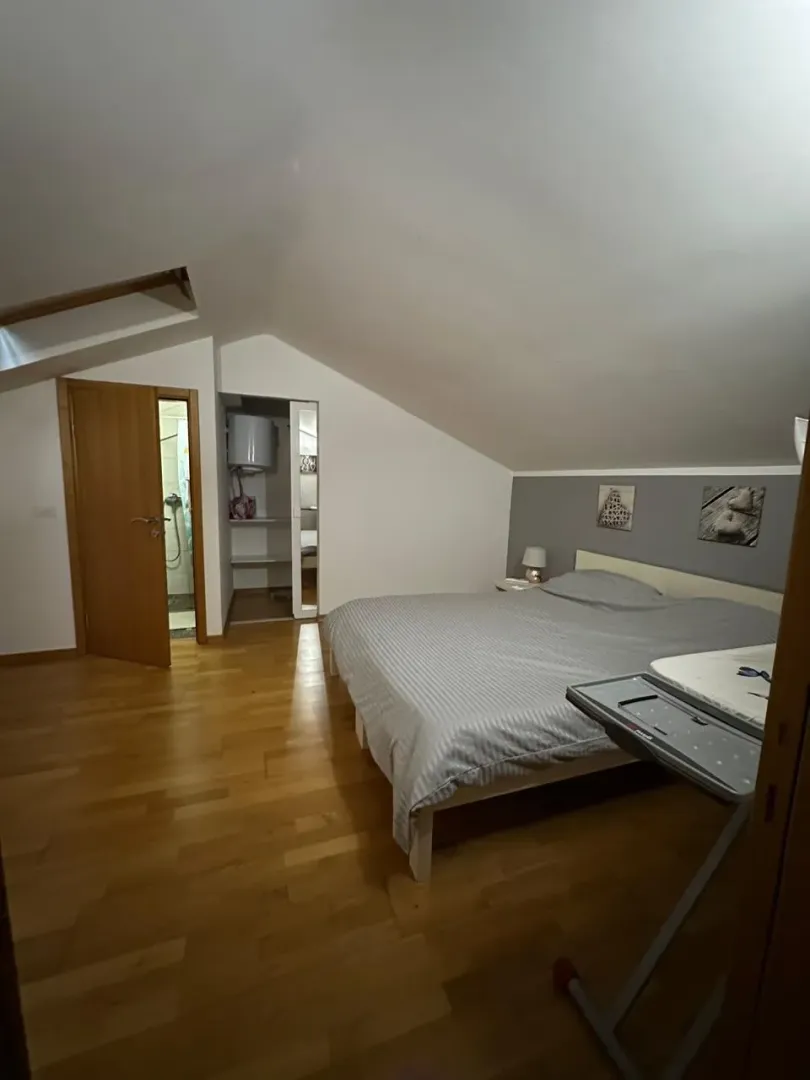 Potkrovna spavaća soba sa bračnim krevetom, drvenim podom i sopstvenim kupatilom.