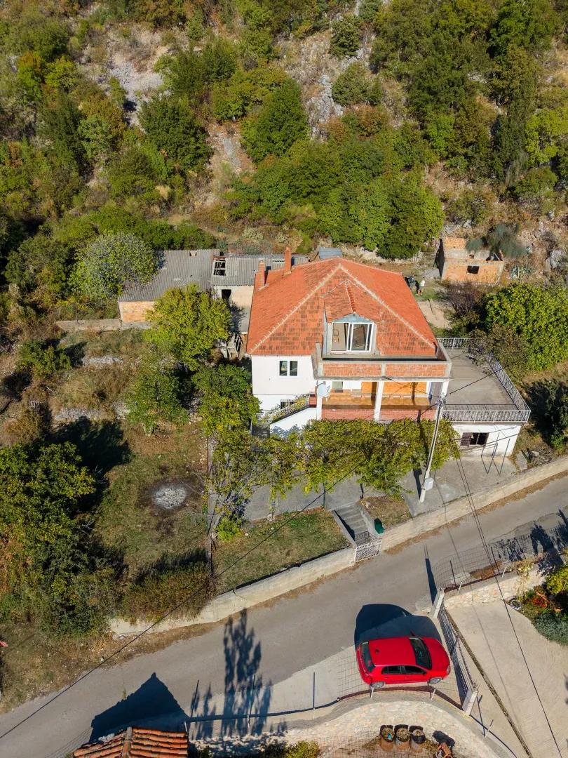 Pogled iz vazduha na kuću sa crvenim krovom i dvorištem.