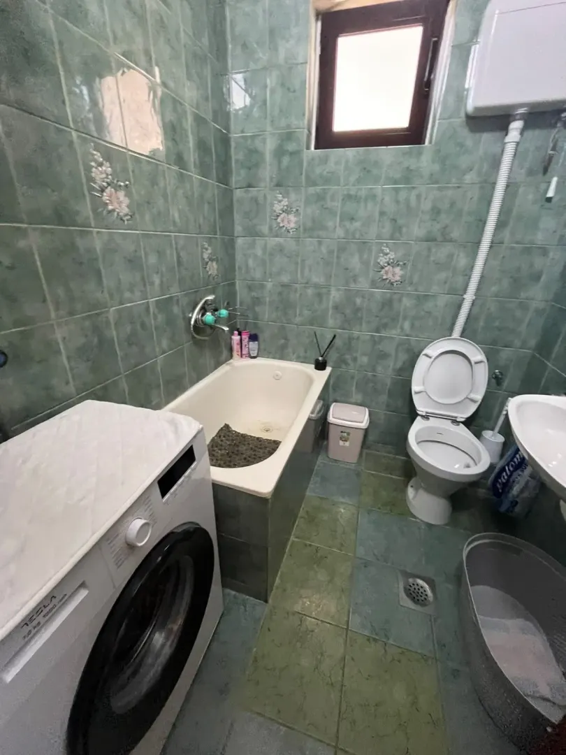 Kupatilo obloženo zelenim pločicama sa kadom, wc šoljom, umivaonikom i mašinom za veš.