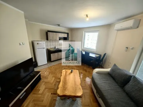 Living room with a sofa, TV, and a kitchen in the background. - image 2