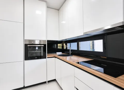 Modern white kitchen with a wooden countertop and built-in oven. - image 5