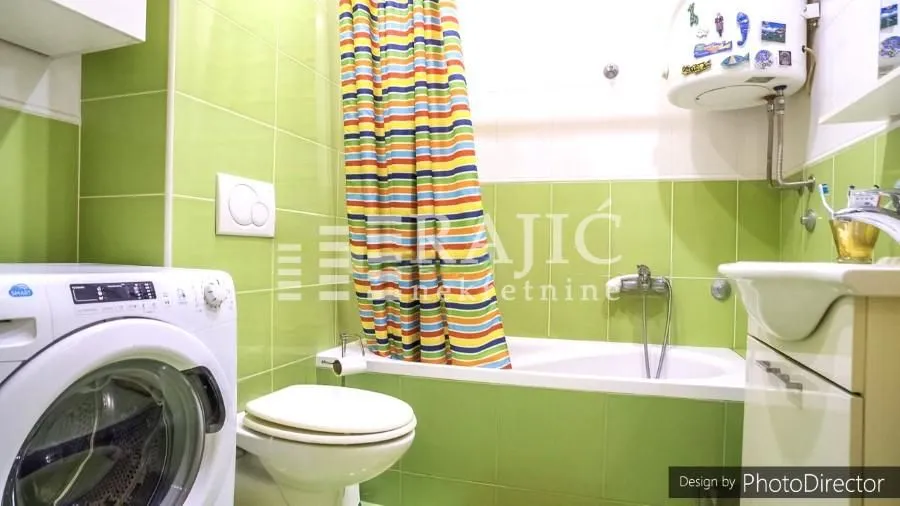 Manje kupatilo sa kadom, umivaonikom i veš mašinom u zelenim pločicama.