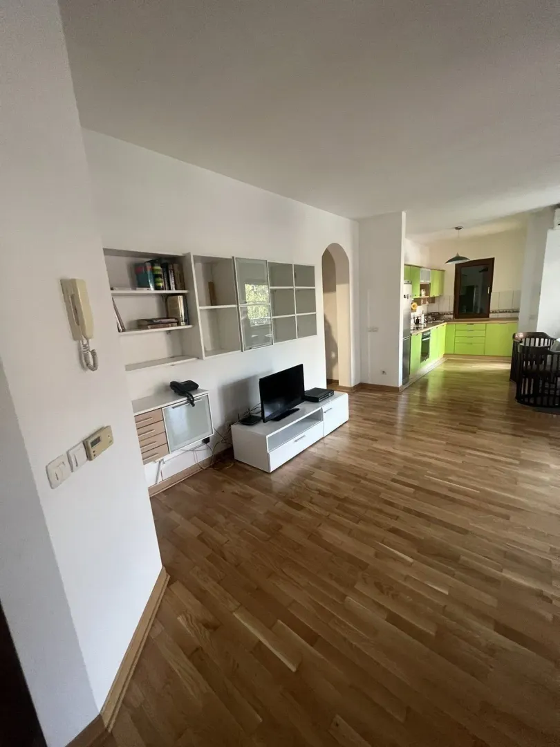 Bright living room with wooden flooring opening into a green kitchen.