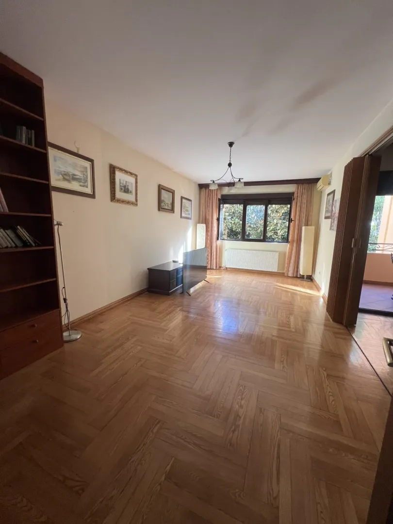 Spacious living room featuring parquet flooring, a bookshelf, and balcony access.