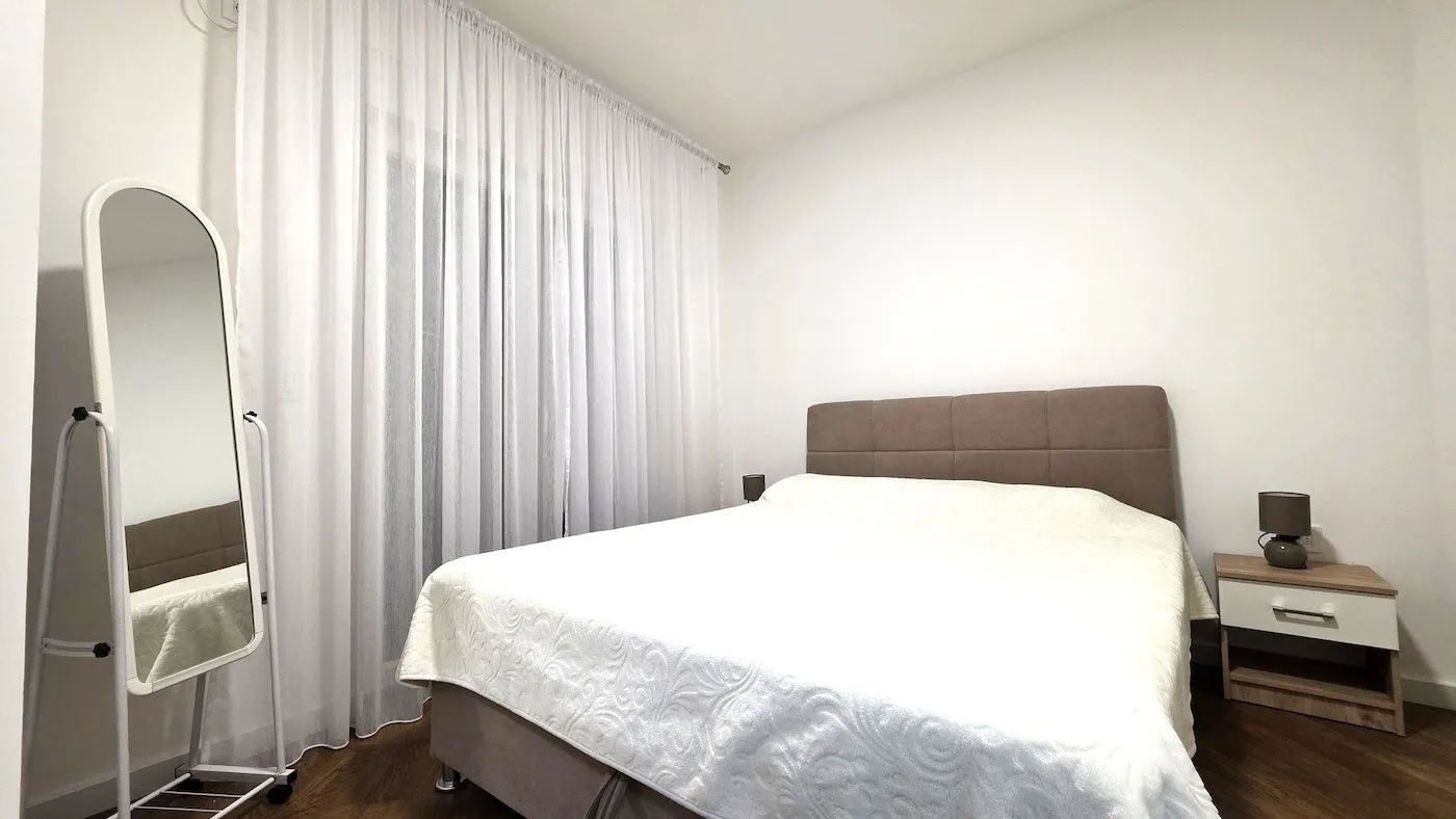 Bright and tidy bedroom with a double bed, nightstand, and mirror.