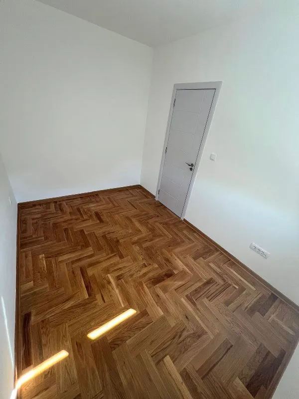 Empty room with wooden parquet flooring and white walls.