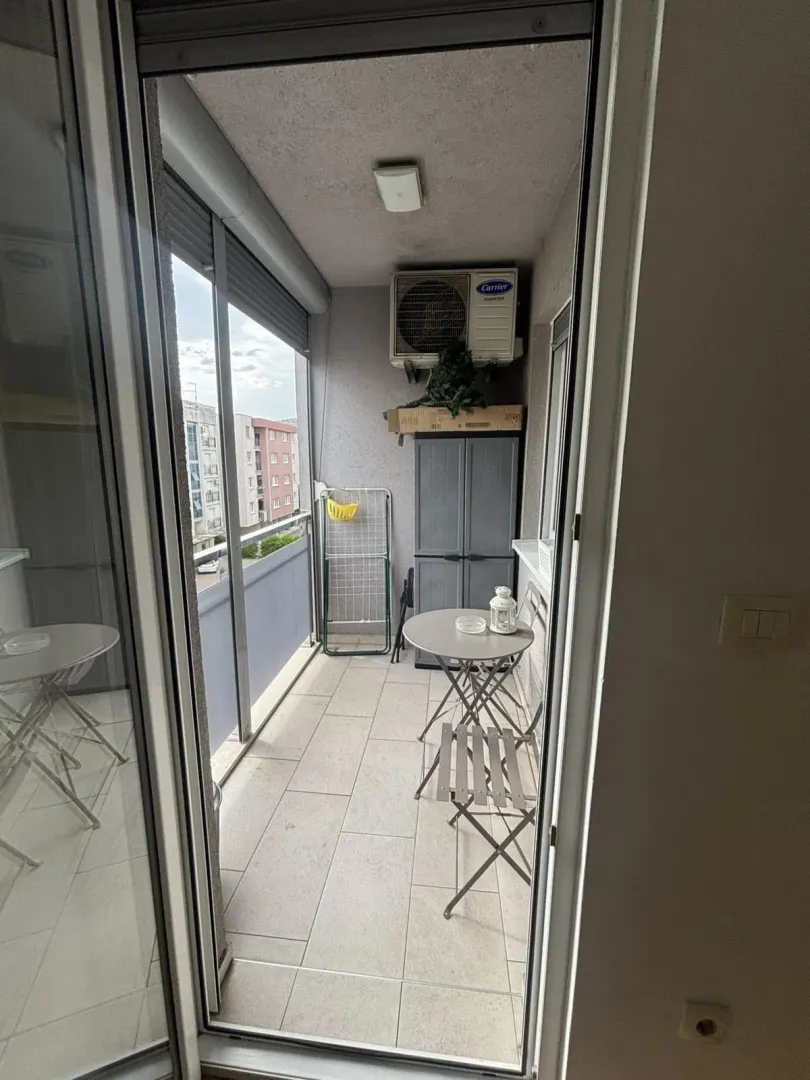 Pogled na zastakljeni balkon sa malim stolom, stolicama i klima uređajem.