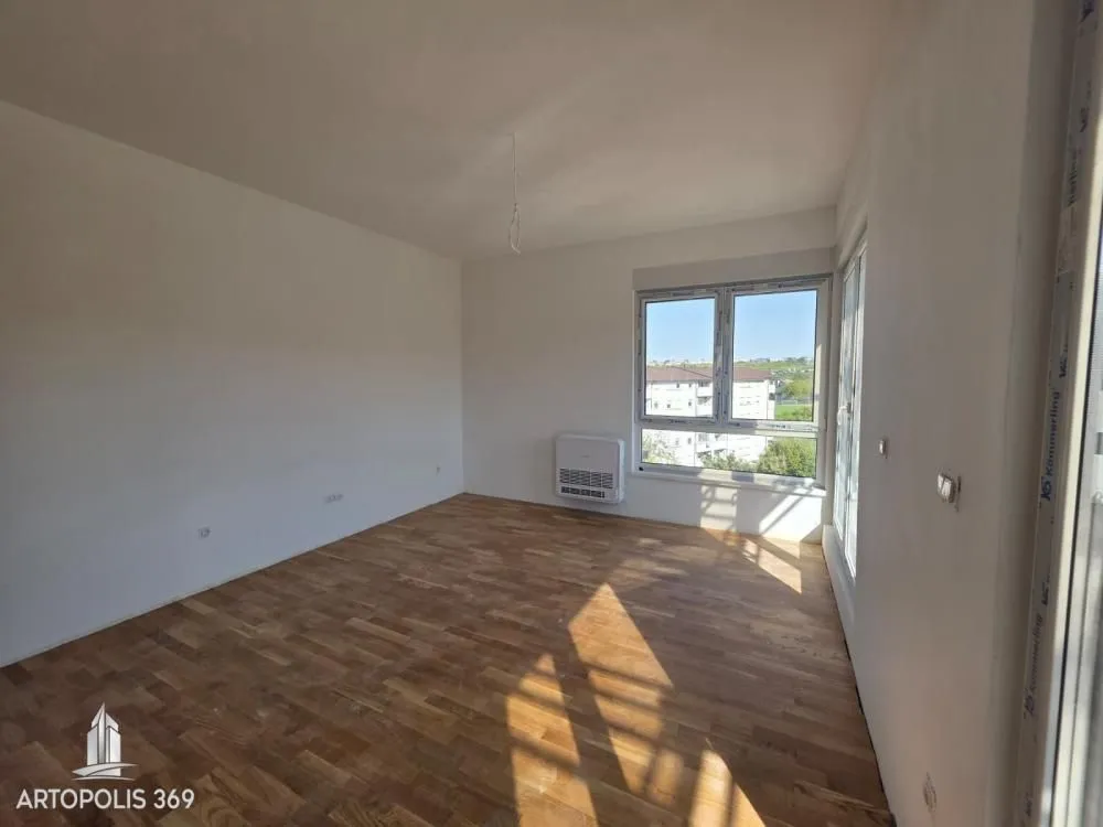 Empty unfinished room with wooden flooring and windows.