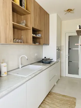 Moderna kuhinja sa bijelim radnim površinama i drvenim visećim elementima. - image 6