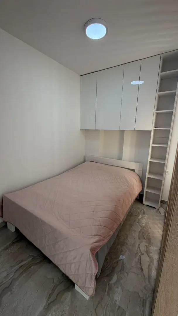 Manja spavaća soba sa bračnim krevetom, ugradnim plakarom i bijelim elementima.