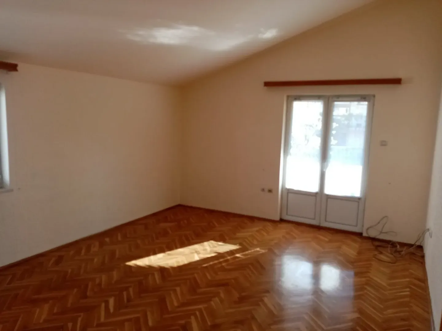 An empty room with parquet flooring and a balcony door.