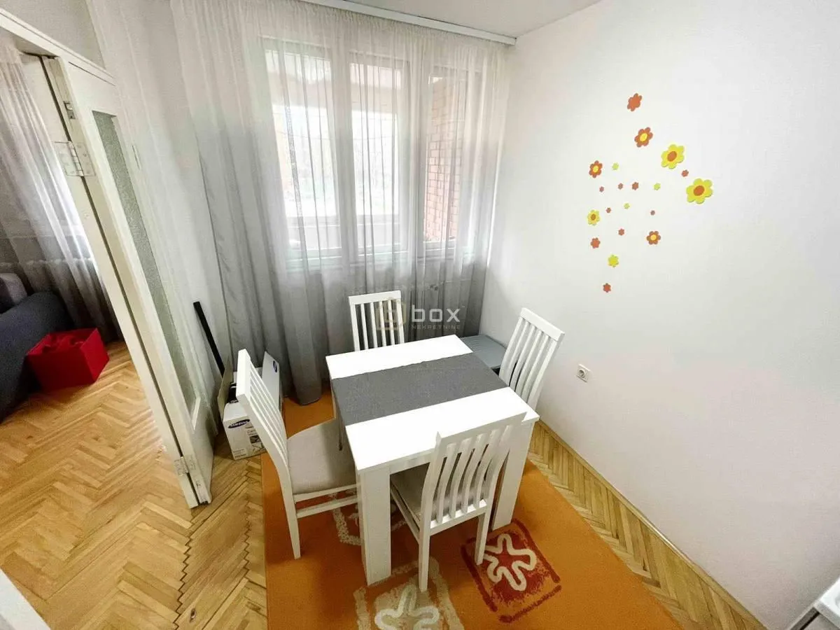 Manja trpezarija sa stolom i belim stolicama pored prozora.