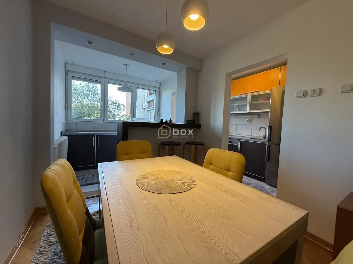 Dining area with a wooden table and yellow chairs, overlooking the kitchen and enclosed area.