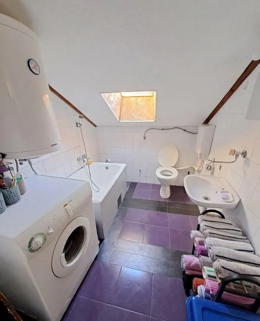 Manje kupatilo sa kadom, wc šoljom, umivaonikom i mašinom za veš pod krovnim kosinama.
