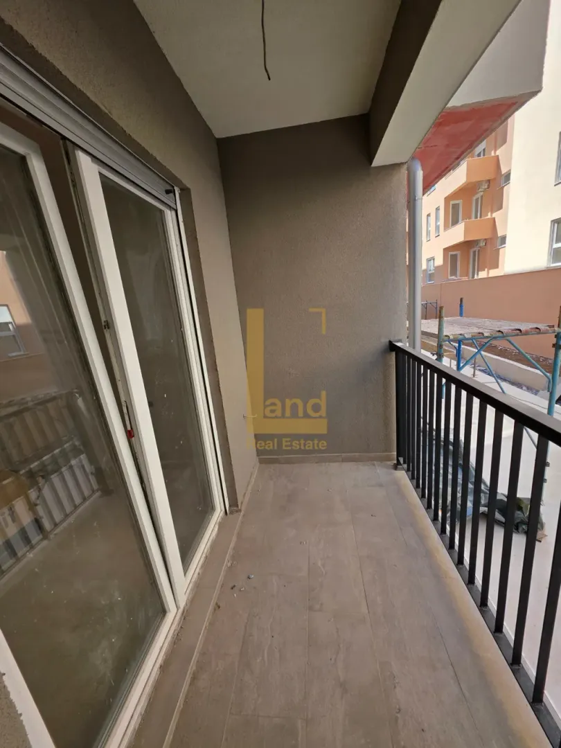 Prazan nenamješten balkon sa crnom ogradom i staklenim balkonskim vratima.