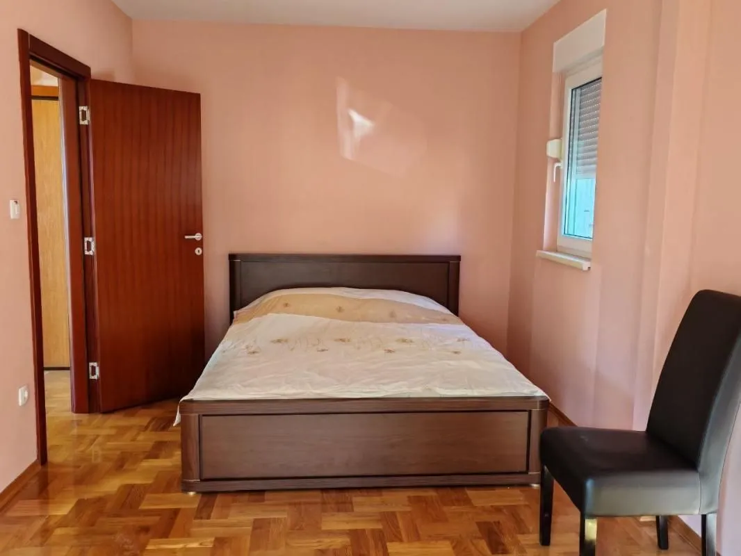 Spavaća soba sa bračnim krevetom, drvenim parketom i vratima koja vode u hodnik.