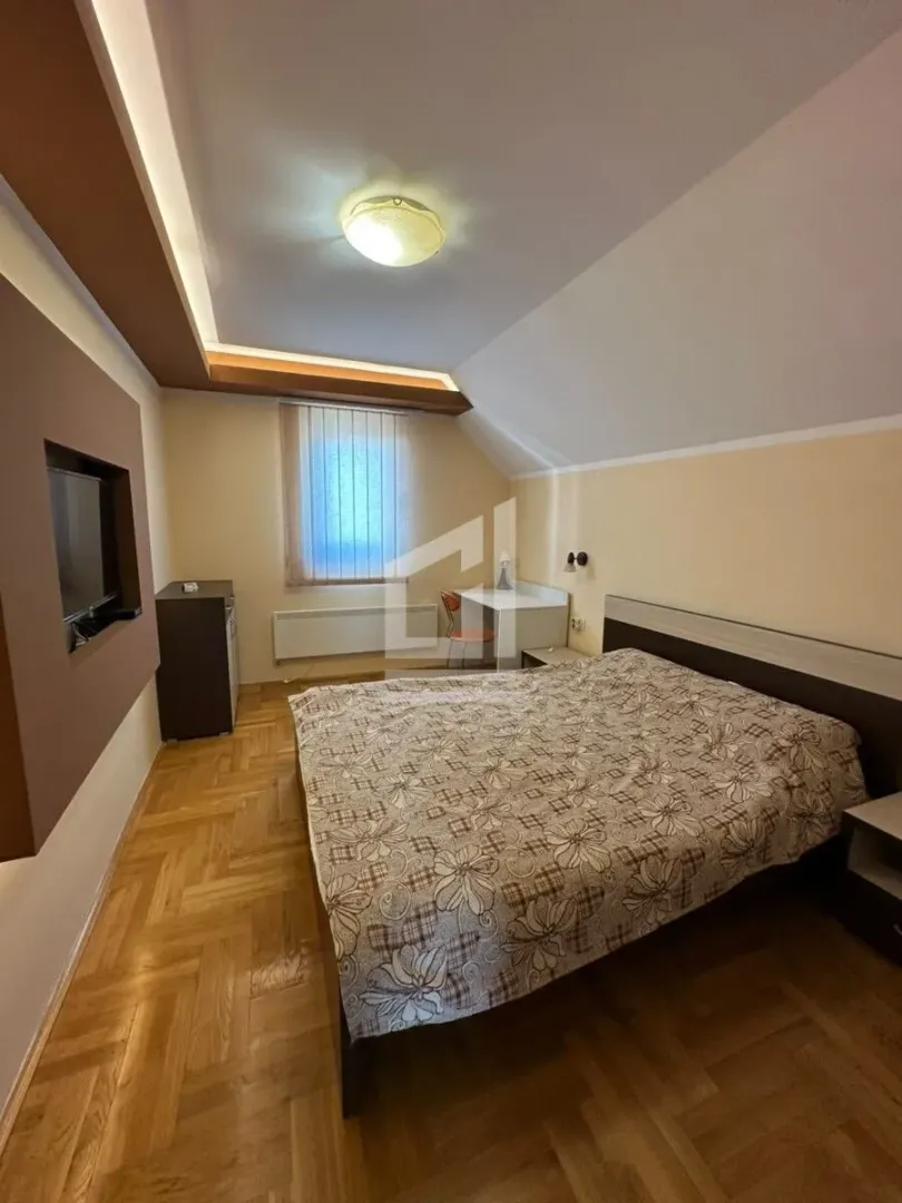 Namještena spavaća soba sa bračnim krevetom, radnim stolom i TV-om na zidu.