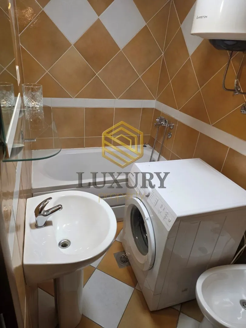 Smaller bathroom with a bathtub, washbasin, and washing machine.