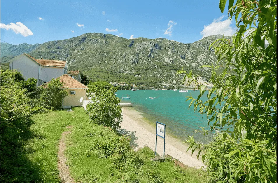 Pogled na dvorište kuće uz obalu mora i planine u pozadini.