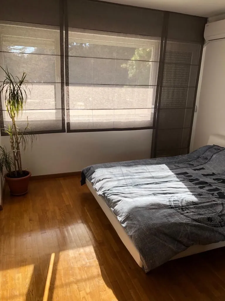 Svijetla spavaća soba sa velikim prozorom, bračnim krevetom i parketom.