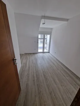 Prazna soba sa bijelim zidovima, drvenim podom i balkonskim vratima. - image 5