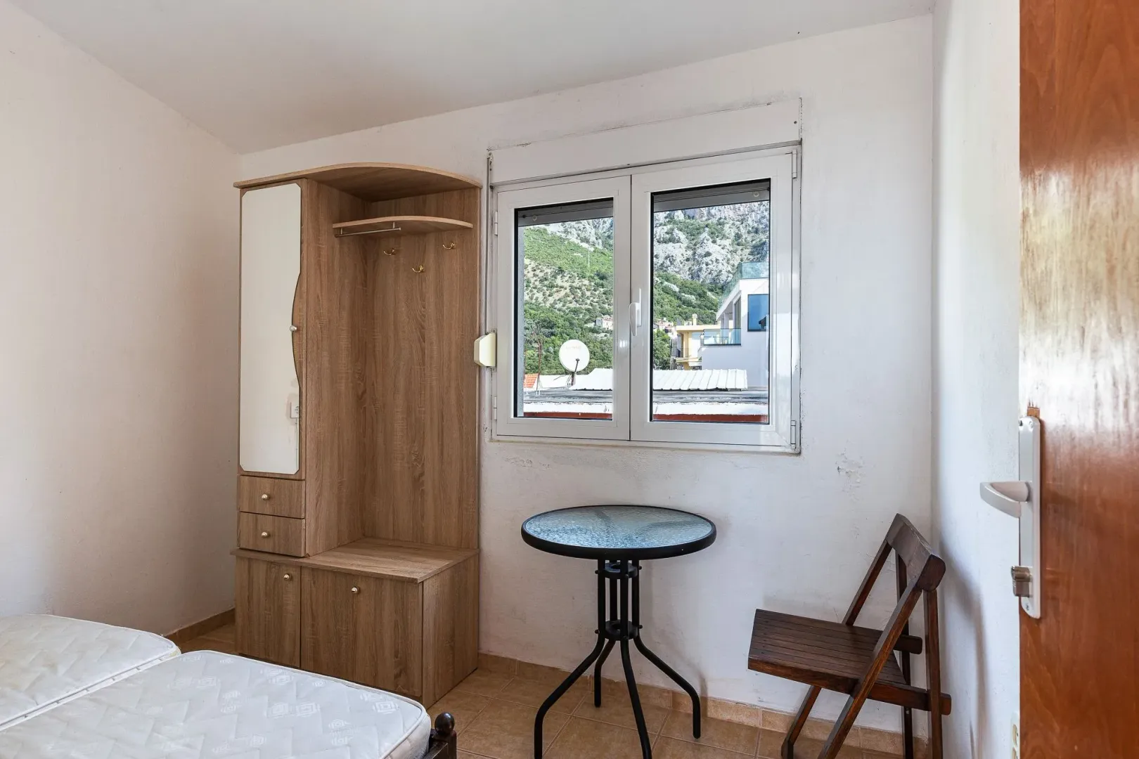 Manja soba sa krevetom, drvenim garderoberom, stočićem i prozorom sa pogledom na planinu.