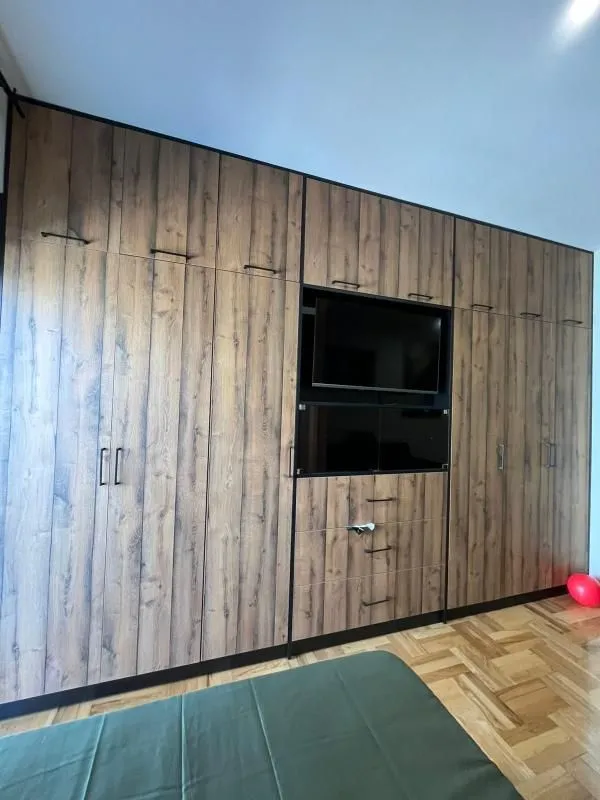 Spavaća soba sa velikim drvenim ormarom i ugrađenim televizorom.