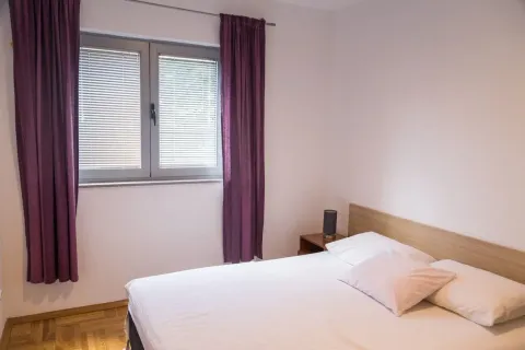 Spavaća soba sa bračnim krevetom i prozorom sa ljubičastim zavjesama. - image 13