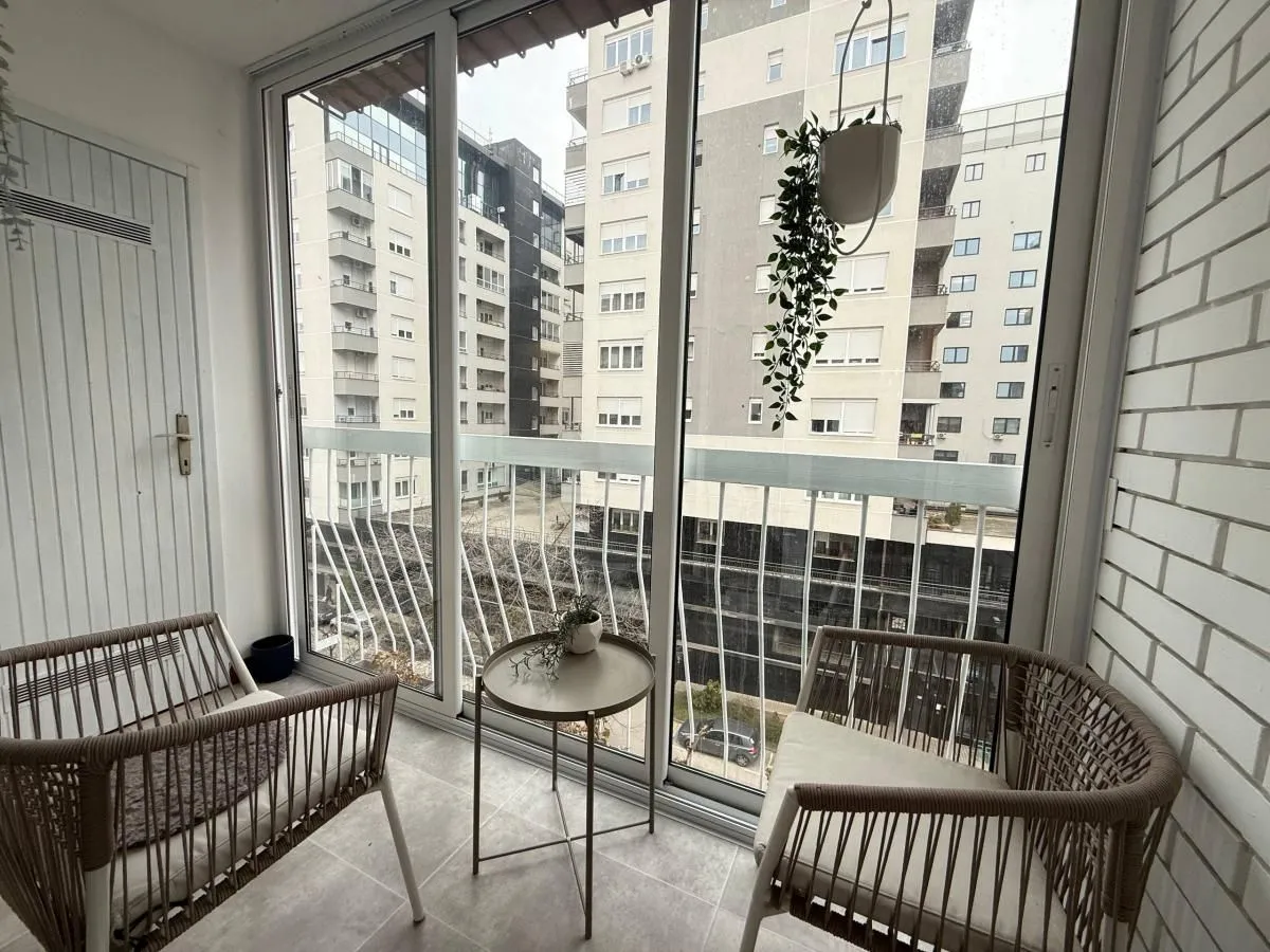 Zastakljeni balkon sa garniturom za sedenje i pogledom na grad.