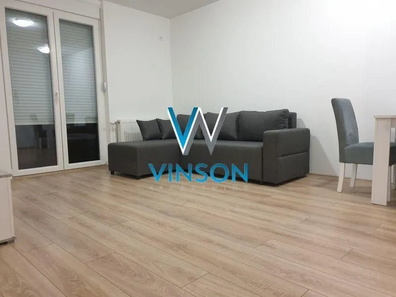 Dnevna soba sa sivom ugaonom garniturom i trpezarijskim stolom.