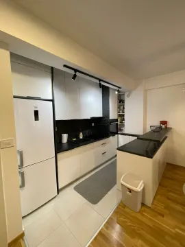 Moderna kuhinja sa bijelim elementima, tamnim radnim površinama i šankom. - image 14