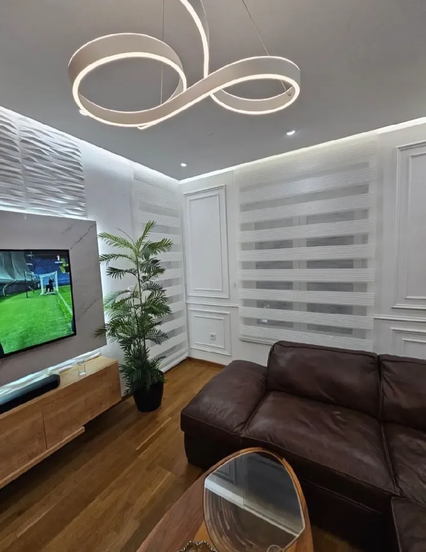 Living room with leather sofa, TV and modern lighting.