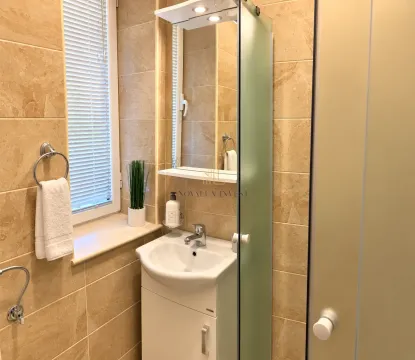 Kupatilo obloženo bež pločicama sa umivaonikom, ogledalom i prozorom. - image 8
