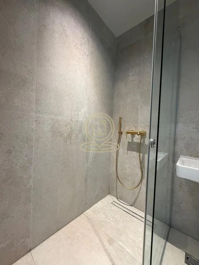 Modern shower cabin with grey tiles and gold-colored faucet.