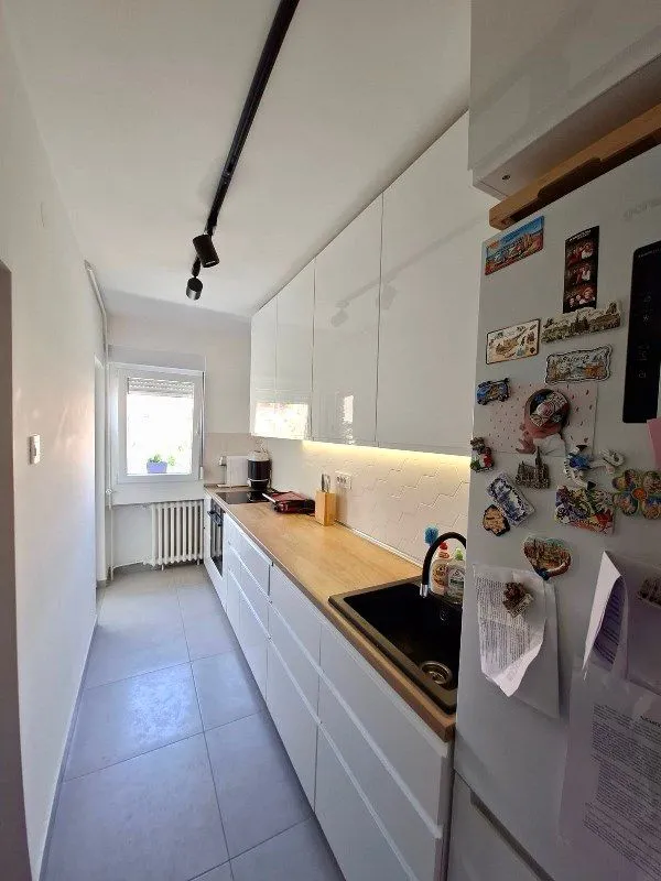 Modern white kitchen with a wooden countertop and a refrigerator.