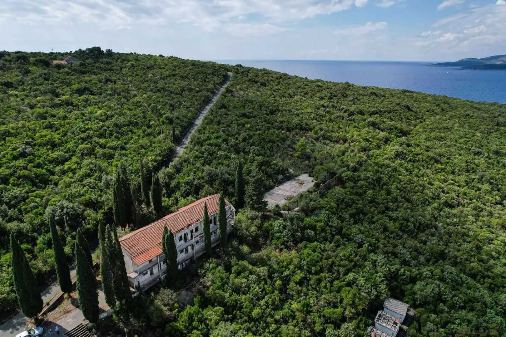 Pogled iz vazduha na staru kuću okruženu šumom i zelenilom blizu mora.