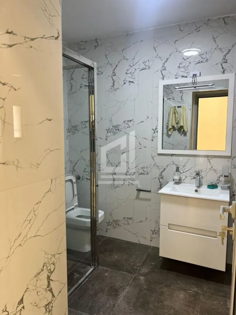 Modern bathroom with a walk-in shower, washbasin, and marble tiles.