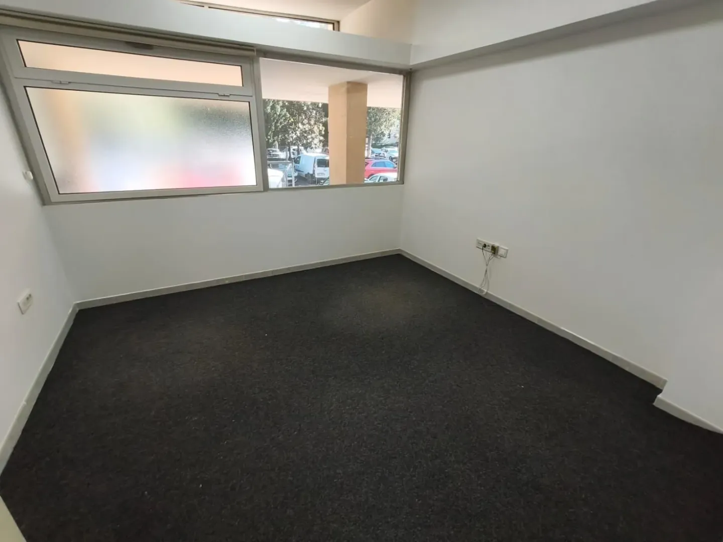 Empty office space with dark carpet and windows facing outside.