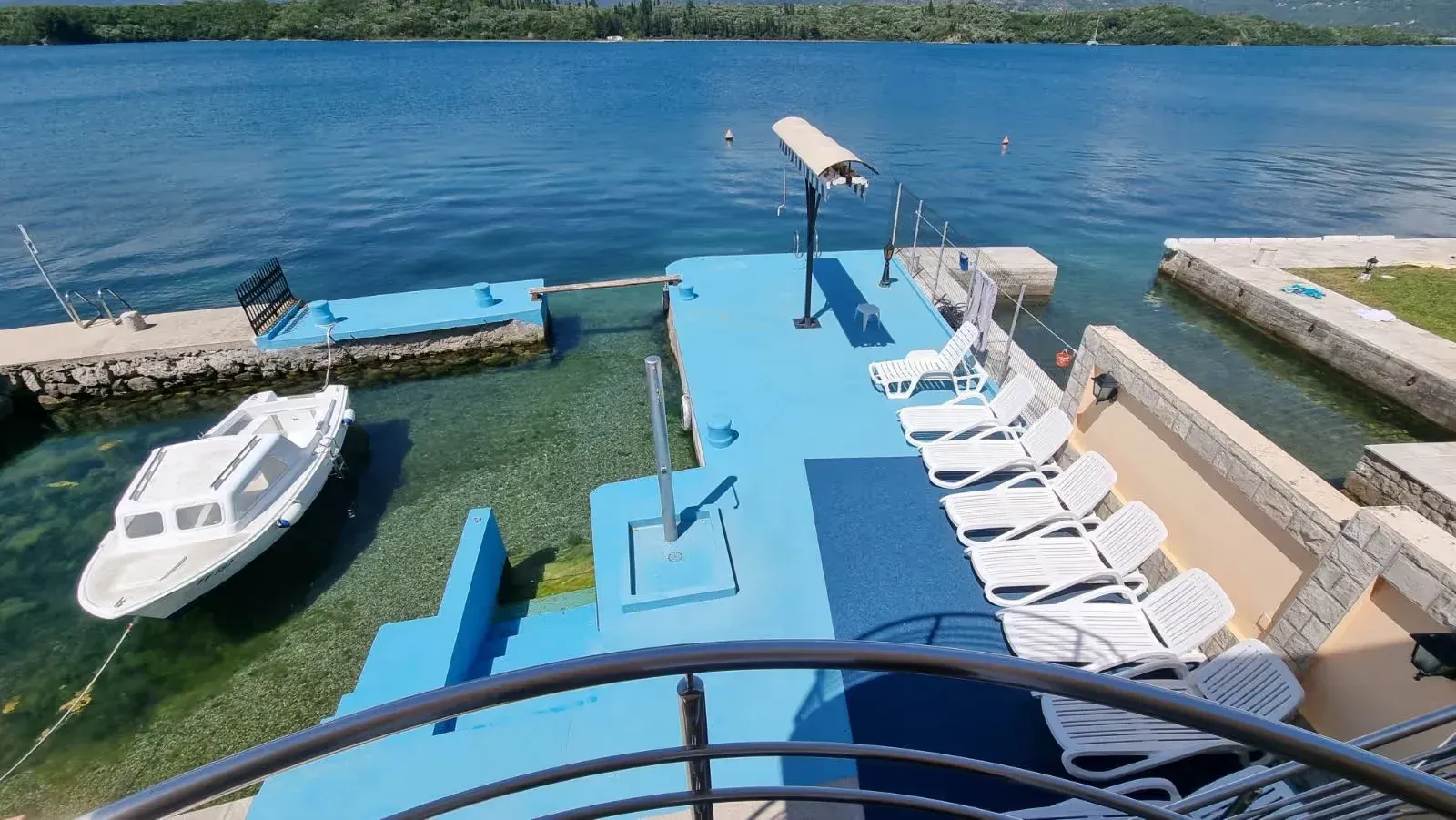Pogled na privatnu betonsku plažu sa ležaljkama i privezanim čamcem.