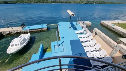 Pogled na privatnu betonsku plažu sa ležaljkama i privezanim čamcem. - image 10