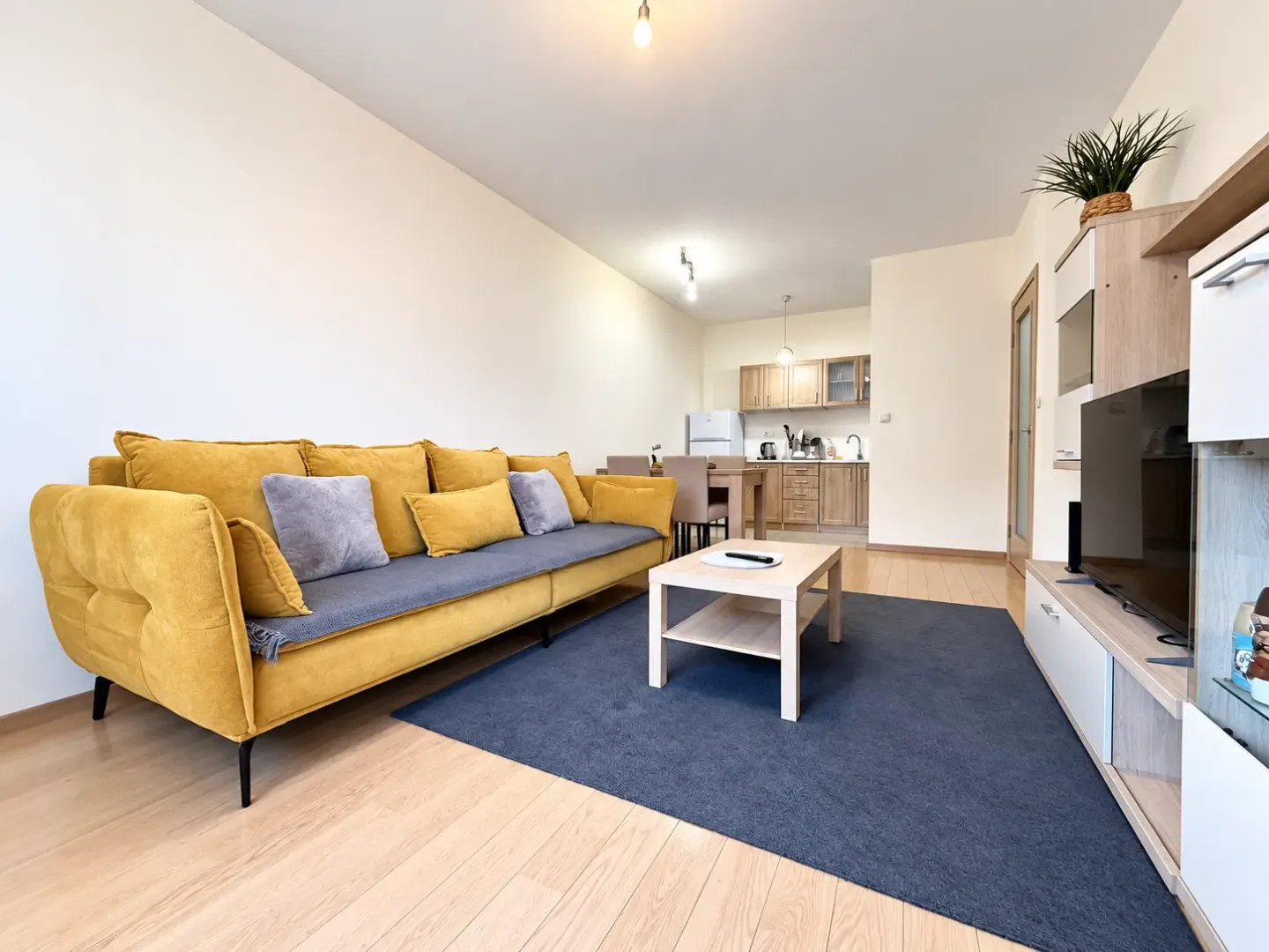 Living room with a yellow sofa and dining area in the background.
